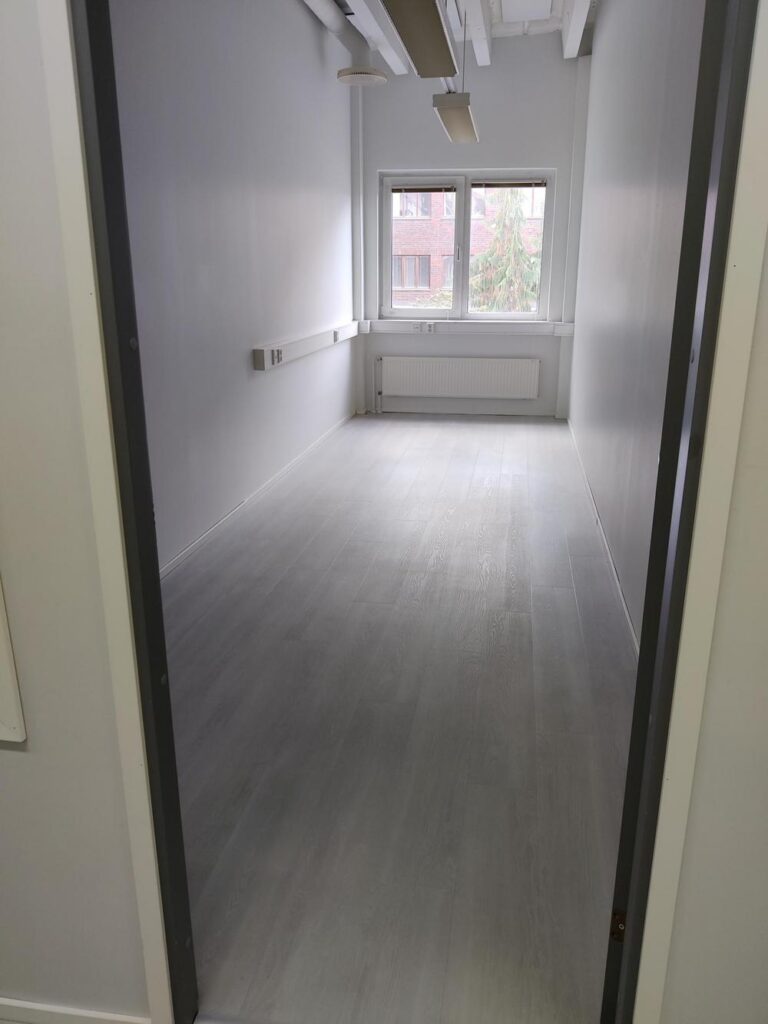 Kuva tyhjästä toimitilasta kahdella ikkunalla. Huone on väriltään valkoinen.