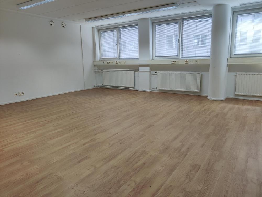 Kuva tyhjästä toimitilasta kuudella ikkunalla. Huoneen seinät ovat valkoiset ja lattia on puinen laminaatti.