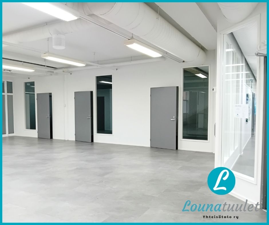 Valokuva toimitilasta, missä avara aula, ovi käytävälle, iso ikkuna ja kolme ovea, joiden vieressä ikkunat.